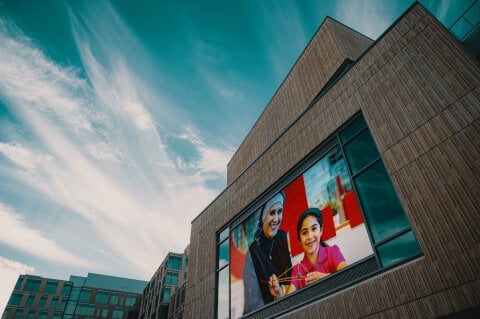 A cement building side with a large programmable digital sign on featuring a mother and child interacting and smiling.