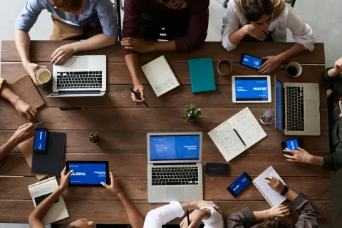 A team coordinating company communication at desk with several computers and notepads.