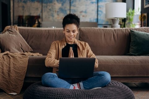 A woman sitting on the couch working on her laptop using a top digital signage platform.