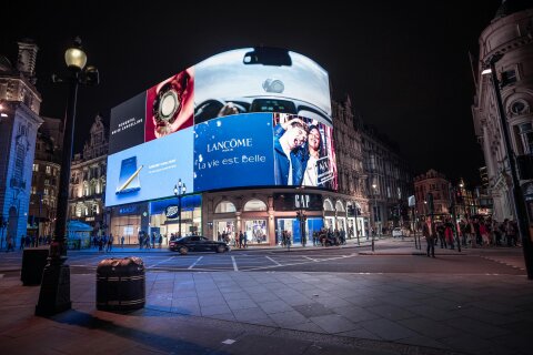 A large digital sign that wraps around the side of a building in a busy public square.